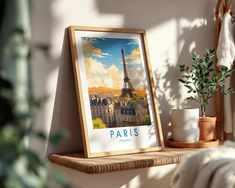 Op de afbeelding: Een ingelijste kunstdruk met een gestileerde illustratie van de Eiffeltoren in Parijs, Frankrijk. De afbeelding toont een stadsgezicht onder een blauwe lucht met gouden wolken, met de tekst PARIS FRANCE in het blauw onderaan de witte rand.