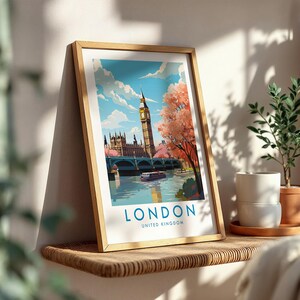 Op de afbeelding: Een ingelijste kunstdruk met een gestileerde illustratie van de skyline van Londen, inclusief de Big Ben, het Parlement en een brug over de Theems. De tekst LONDON UNITED KINGDOM staat in blauw onderaan de witte rand gedrukt.