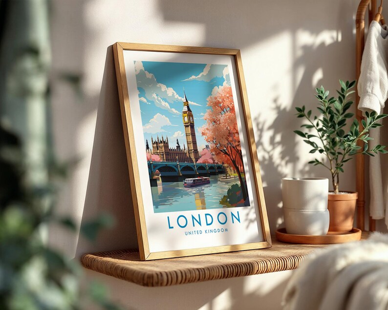 Op de afbeelding: Een ingelijste kunstdruk met een gestileerde illustratie van de skyline van Londen, inclusief de Big Ben, het Parlement en een brug over de Theems. De tekst LONDON UNITED KINGDOM staat in blauw onderaan de witte rand gedrukt.