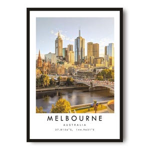 May include: A framed print of the Melbourne, Australia skyline. The image shows a cityscape with modern skyscrapers, a river, and a bridge. The word "MELBOURNE" is printed at the bottom, along with the country and coordinates.