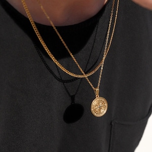 May include: Two gold chains with a compass pendant. The pendant is round and has a detailed design.