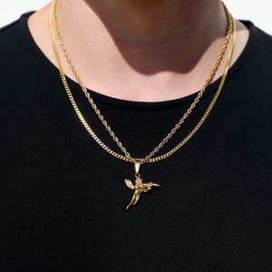 Puede incluir: Un collar de cadena de oro con un colgante de ángel de oro. El collar está superpuesto con una segunda cadena más fina.