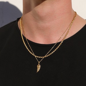 Puede incluir: Un collar de cadena de oro con un peque&ntilde;o colgante de ala de oro. El collar est&aacute; superpuesto a una segunda cadena de oro m&aacute;s fina.