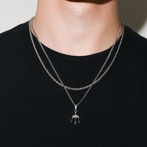 May include: A silver chain necklace with a trident pendant. The necklace is layered with a second, thinner chain.