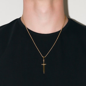 May include: A gold chain necklace with a sword pendant. The chain is a rope style and the pendant is a simple, flat design.