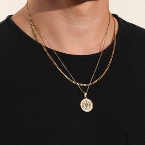 May include: A gold chain necklace with a compass pendant. The chain is layered with a thinner chain.