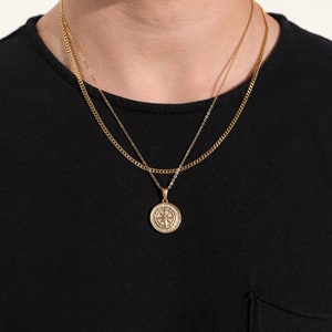 May include: A gold chain necklace with a compass pendant. The chain is layered with a thinner chain.
