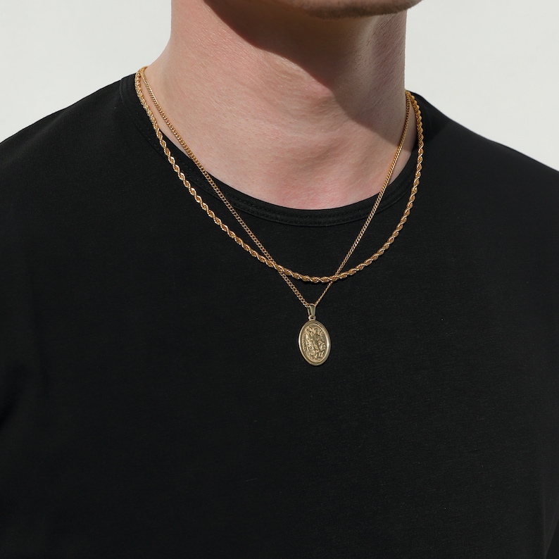 May include: Two gold chains with a pendant featuring a religious figure. The chains are layered and the pendant is oval shaped.
