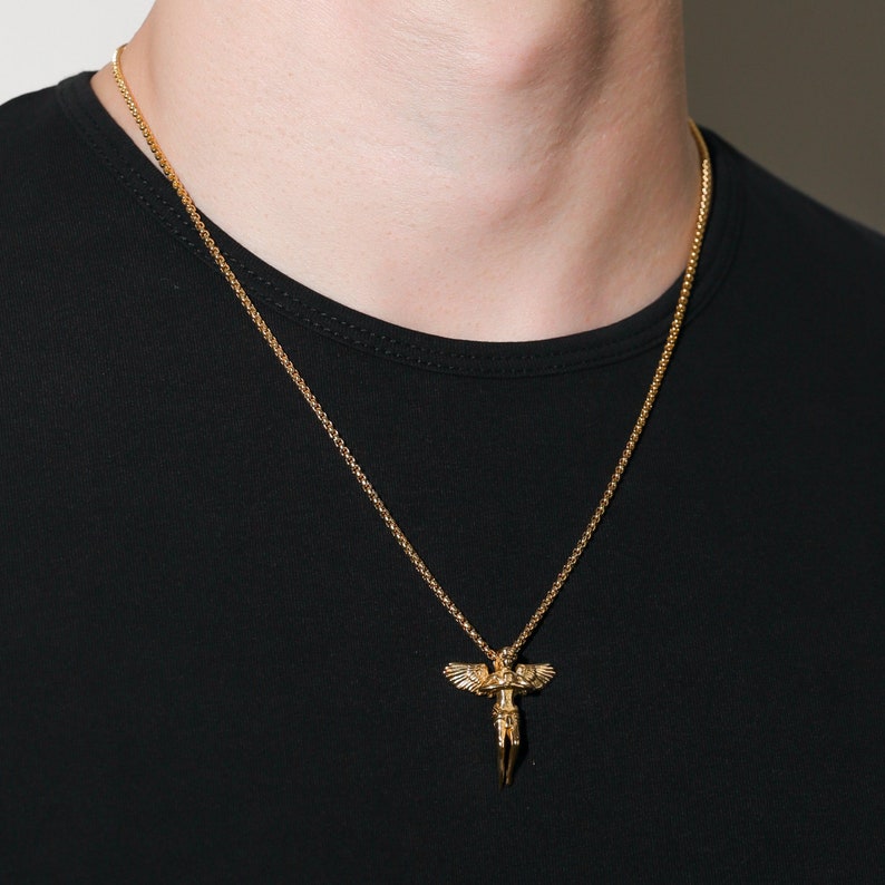 May include: A gold chain necklace with an angel pendant. The angel is depicted with wings outstretched and holding a cross.