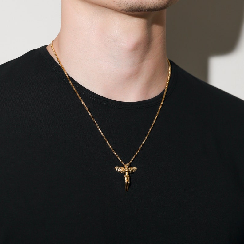 May include: A gold chain necklace with a pendant featuring a detailed angel figure with wings.