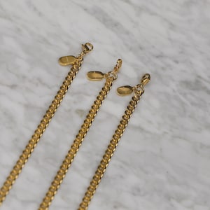 Peut inclure: Trois colliers en cha&icirc;ne dor&eacute;s de longueurs diff&eacute;rentes avec des breloques ovales attach&eacute;es aux extr&eacute;mit&eacute;s.