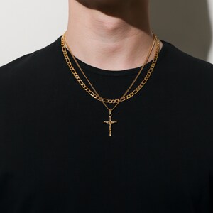 May include: A gold chain necklace with a small gold cross pendant. The necklace is layered with a thicker gold chain.