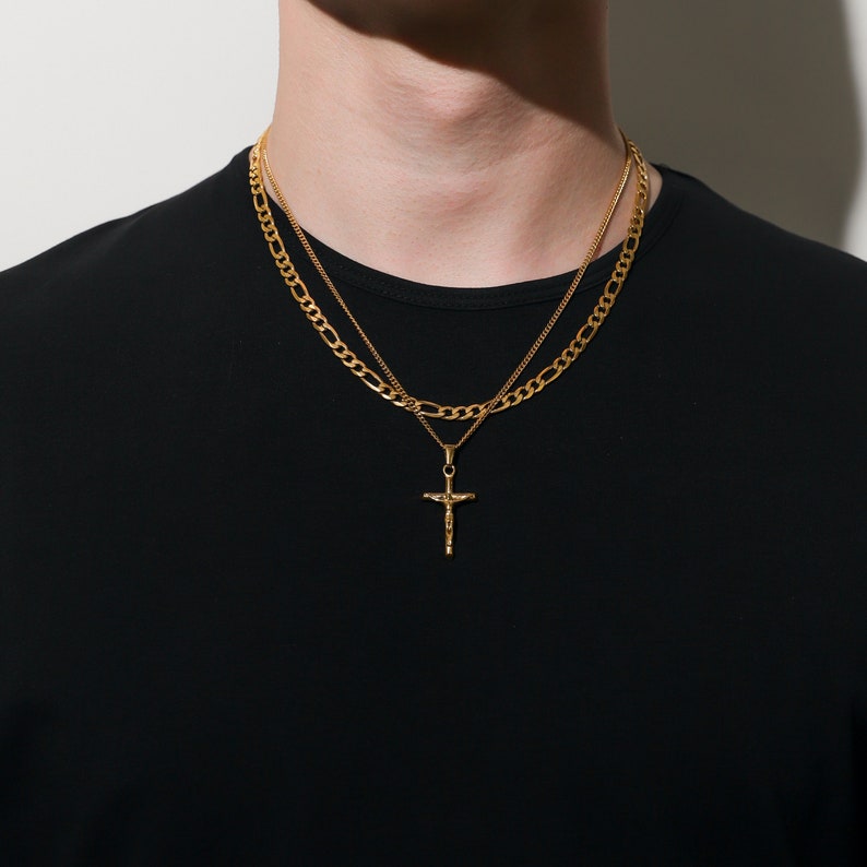 May include: A gold chain necklace with a small gold cross pendant. The necklace is layered with a thicker gold chain.