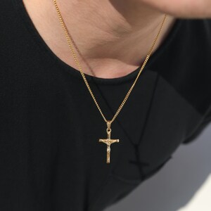 May include: A gold chain necklace with a gold cross pendant featuring a figure of Jesus Christ.
