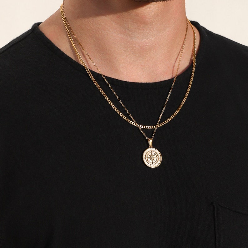 May include: A gold chain necklace with a compass pendant. The chain is layered with a thinner chain.