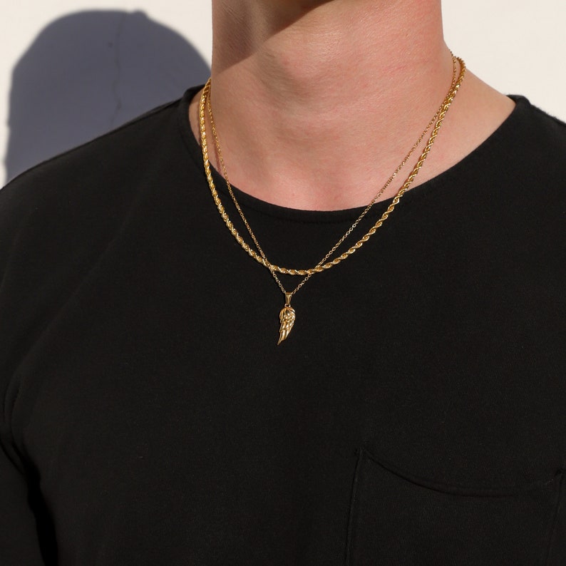 Puede incluir: Un collar de cadena de oro con un peque&ntilde;o colgante de ala de oro. El collar est&aacute; superpuesto a una segunda cadena de oro m&aacute;s fina.