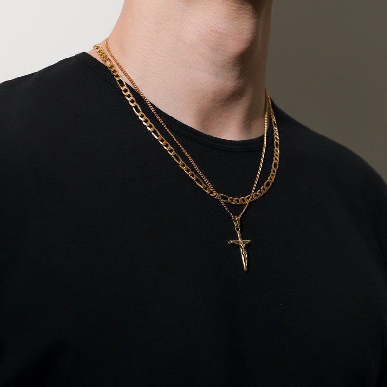 May include: A gold chain necklace with a gold cross pendant. The necklace is layered with a thinner gold chain.