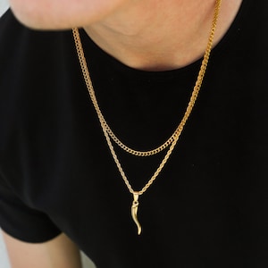 K&ouml;nnte beinhalten: Eine goldene Kettenkette mit einem goldenen Hornanh&auml;nger. Die Kette ist mit einer dickeren Kette &uuml;bereinander gelegt.