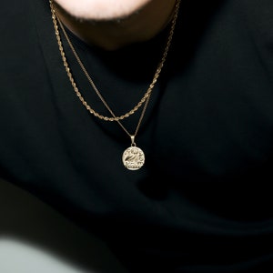 May include: A gold chain necklace with a gold coin pendant. The coin has an inscription on it.