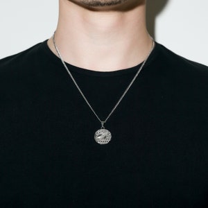 May include: A silver chain necklace with a round pendant featuring a detailed design. The pendant has a raised image of an owl with text around the edge.