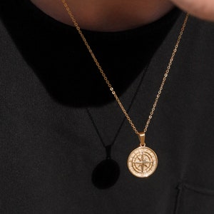 May include: A gold chain necklace with a compass pendant. The compass is round and has a gold finish with a white center and black markings.