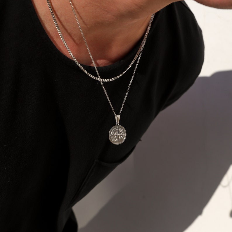 May include: A silver chain necklace with a round pendant featuring a detailed design. The pendant is hanging on a silver chain.