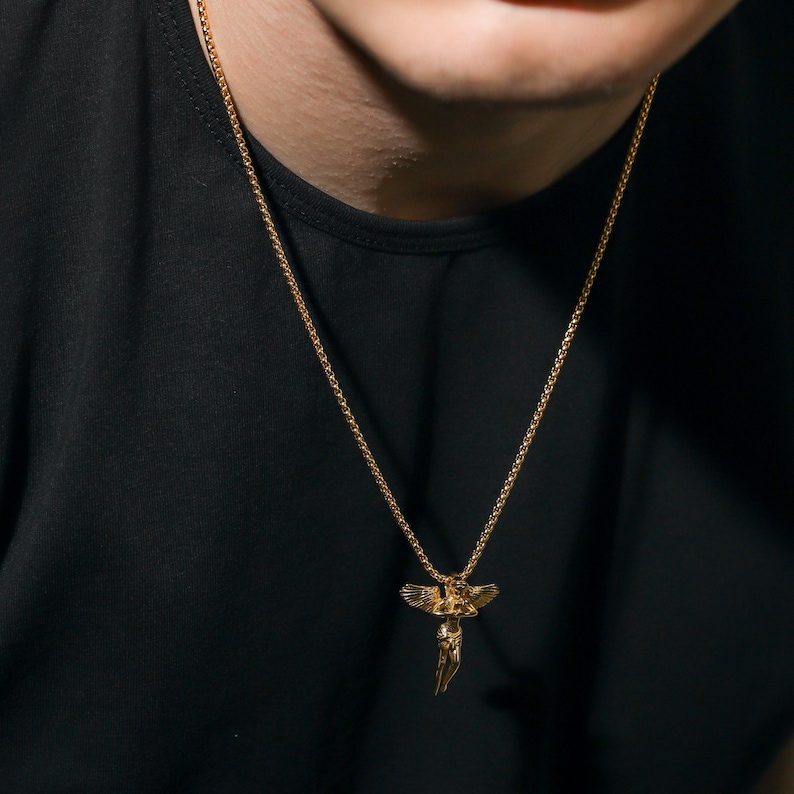 May include: A gold chain necklace with a pendant featuring a winged angel figure.