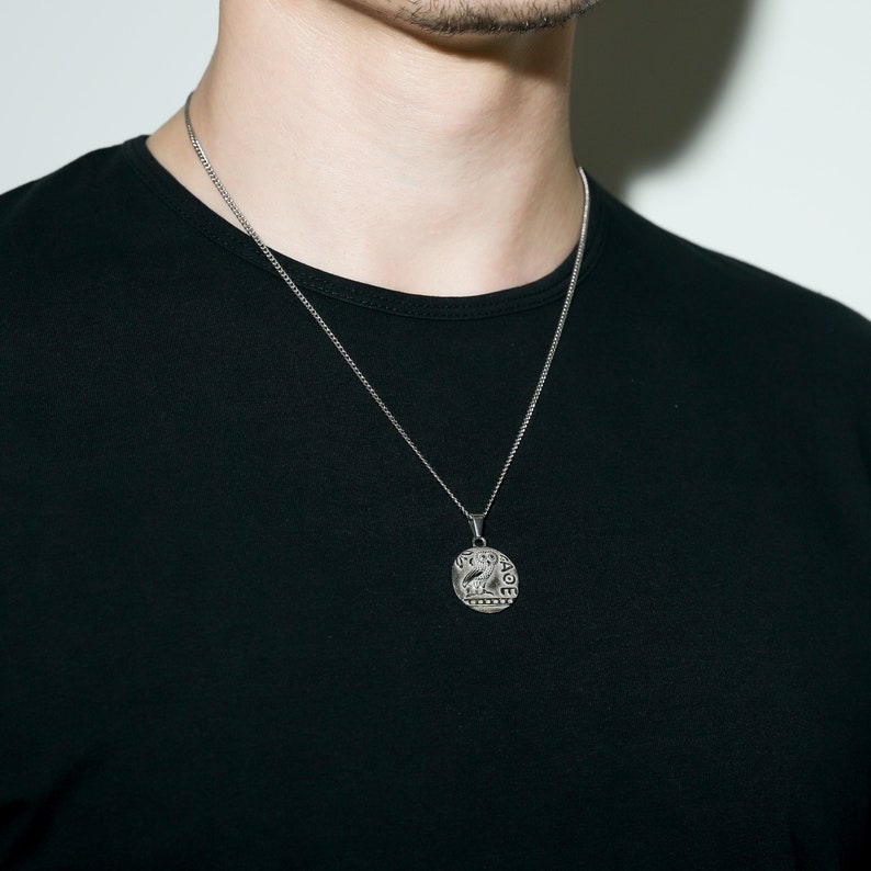 May include: A silver chain necklace with a round pendant featuring a detailed design. The pendant has the word "GRACE" inscribed around the edge.