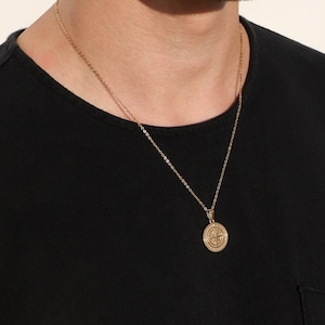 May include: A gold chain necklace with a compass pendant. The compass is round and has a detailed design.