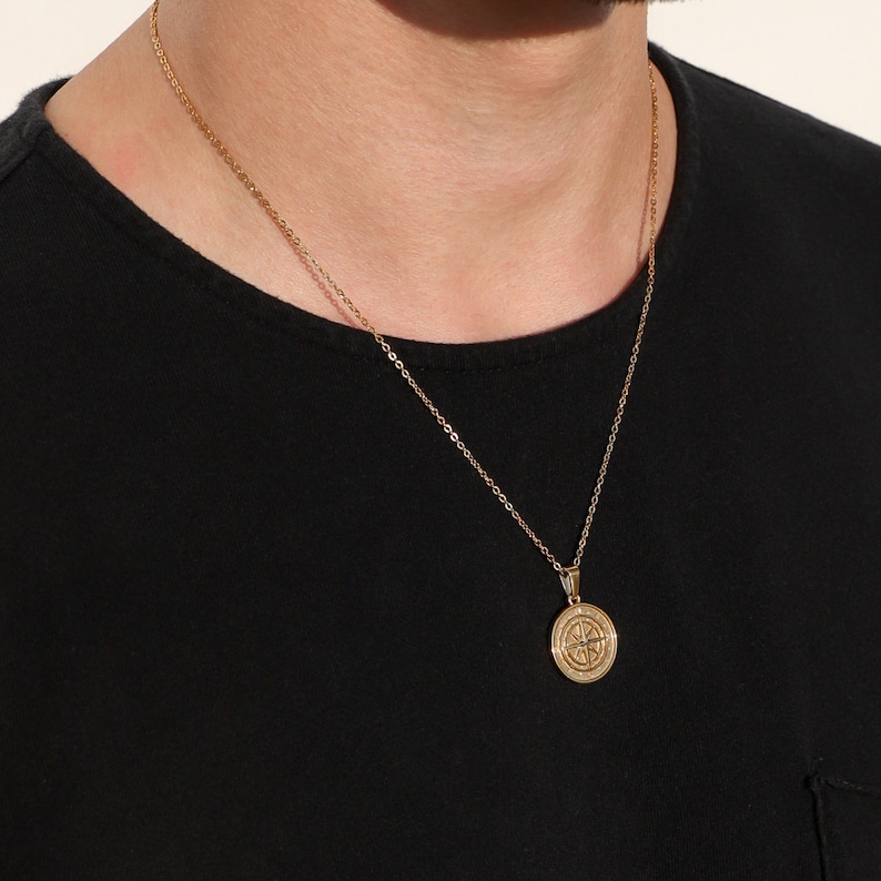 May include: A gold chain necklace with a compass pendant. The compass is round and has a detailed design.
