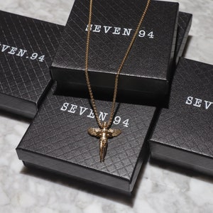 May include: A gold chain necklace with an angel pendant, displayed on black boxes with the text "SEVEN 94" printed on them.