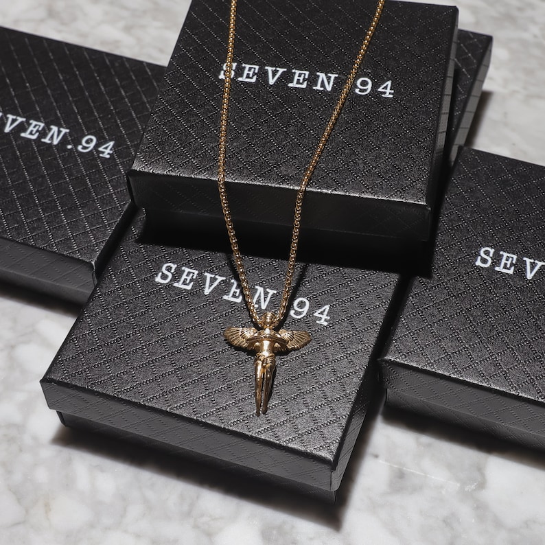 May include: A gold chain necklace with an angel pendant, displayed on black boxes with the text "SEVEN 94" printed on them.