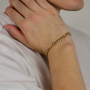 Peut inclure: Un bracelet en cha&icirc;ne dor&eacute;e avec un design de maillons plats. Le bracelet est port&eacute; au poignet.