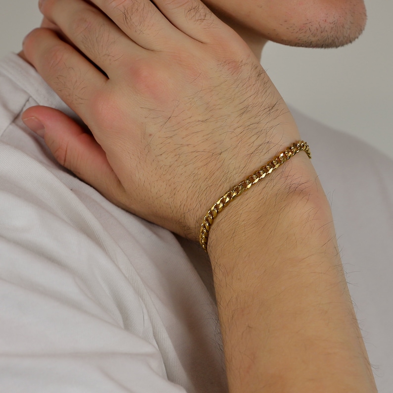 Peut inclure: Un bracelet en cha&icirc;ne dor&eacute;e avec un design de maillons plats. Le bracelet est port&eacute; au poignet.