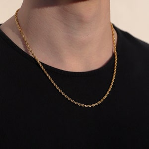 Puede incluir: Un collar de cadena de cuerda de tono dorado en una persona que lleva una camisa negra.