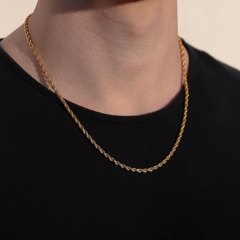 Puede incluir: Un collar de cadena de cuerda de tono dorado en una persona que lleva una camisa negra.
