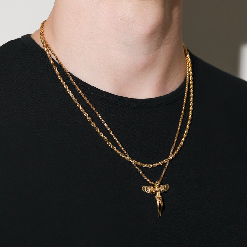 May include: A gold chain necklace with a gold angel pendant. The necklace is layered with a second, thinner chain.