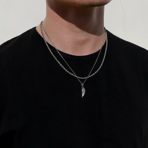 Puede incluir: Un collar de cadena de plata con un colgante de ala de plata. El collar est&aacute; superpuesto con una segunda cadena m&aacute;s fina.