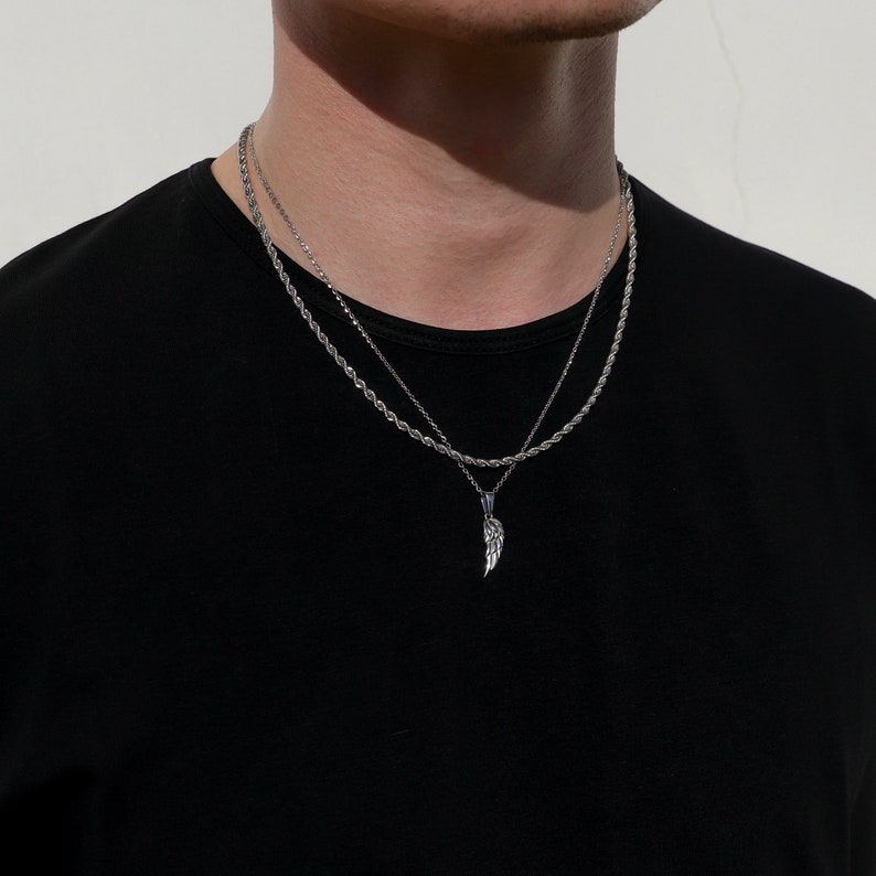 Puede incluir: Un collar de cadena de plata con un colgante de ala de plata. El collar est&aacute; superpuesto con una segunda cadena m&aacute;s fina.