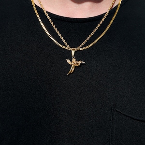 Puede incluir: Un collar de cadena de oro con un peque&ntilde;o colgante de &aacute;ngel. El collar est&aacute; superpuesto con una segunda cadena m&aacute;s gruesa.