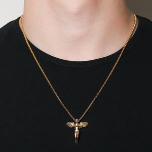 May include: A gold chain necklace with a pendant featuring a detailed angel figure with outstretched wings.