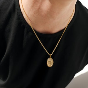 May include: A gold chain necklace with a gold oval pendant featuring a detailed design.