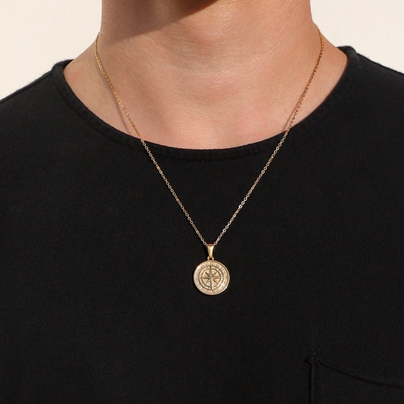 May include: A gold chain necklace with a compass pendant. The compass is round and has a detailed design.
