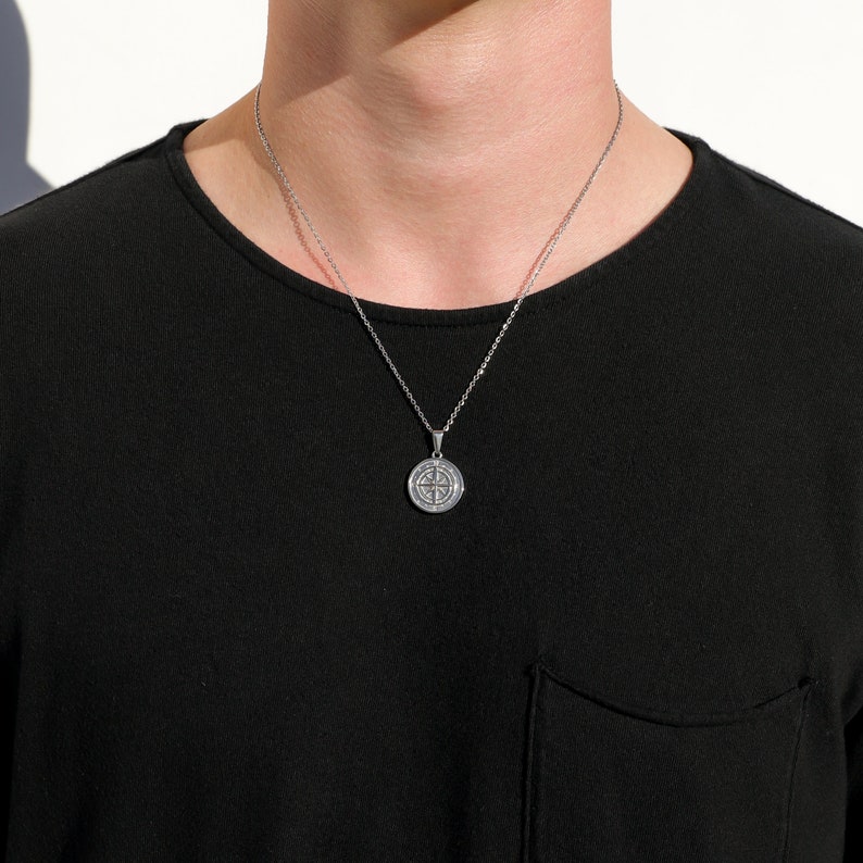 May include: A silver chain necklace with a round pendant featuring a compass design.