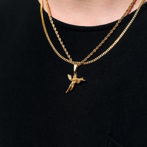 Puede incluir: Un collar de cadena de oro con un colgante de &aacute;ngel de oro. El collar est&aacute; superpuesto a una segunda cadena de oro.