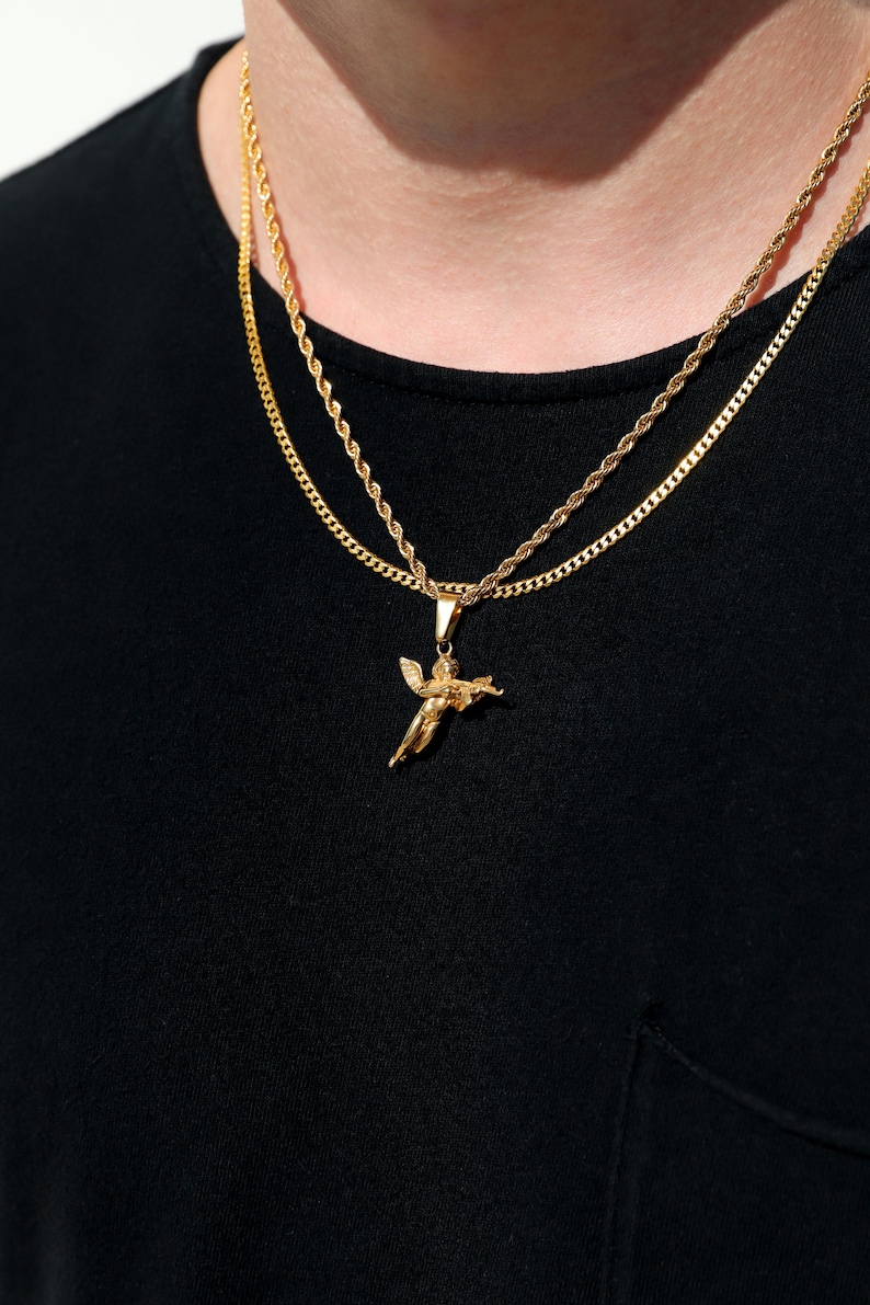 Puede incluir: Un collar de cadena de oro con un colgante de &aacute;ngel de oro. El collar est&aacute; superpuesto a una segunda cadena de oro.