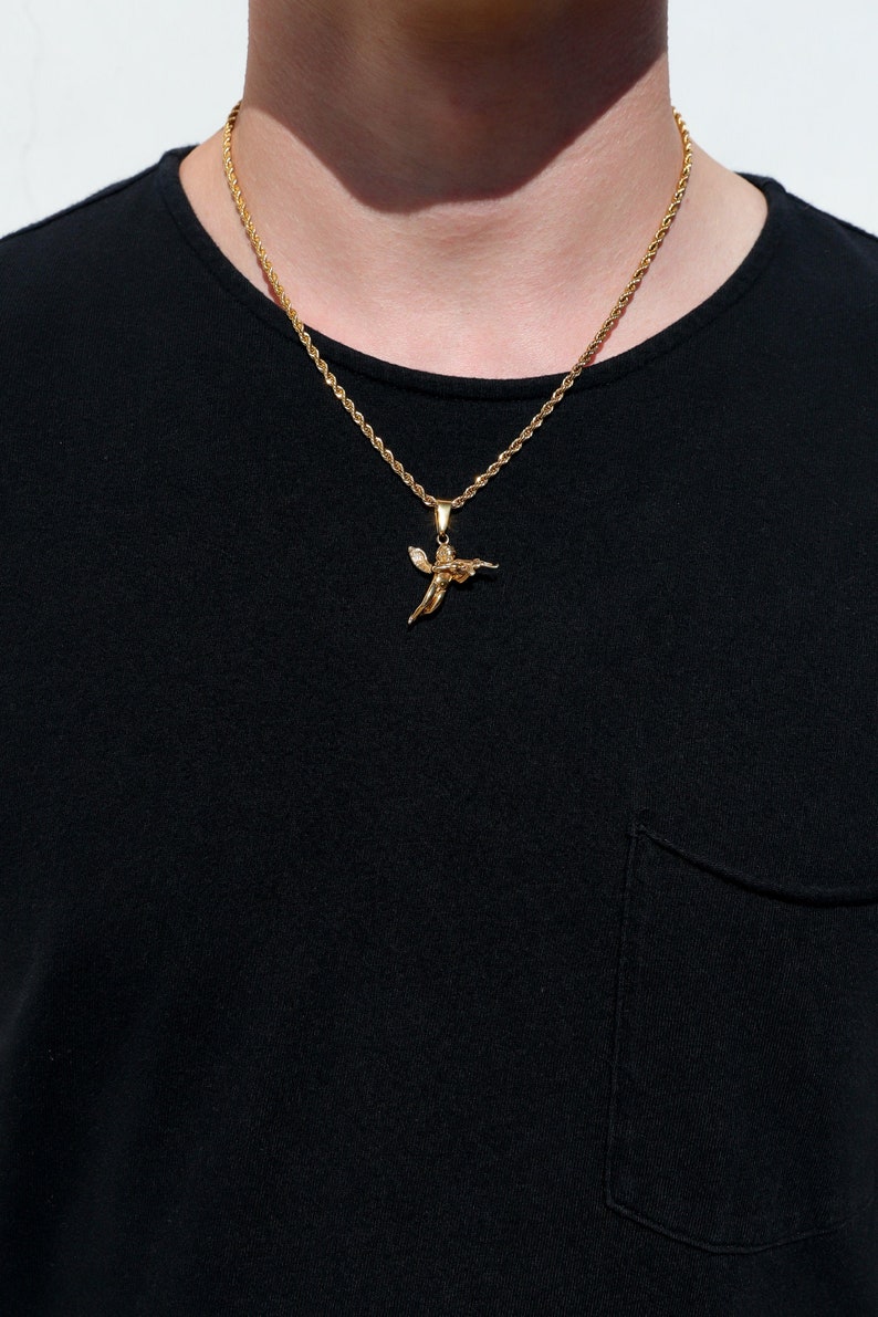 Puede incluir: Un collar de cadena de oro con un peque&ntilde;o colgante de &aacute;ngel. La cadena es de estilo cuerda y el colgante es detallado.