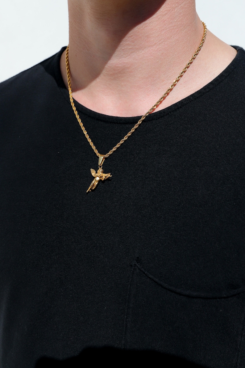 Puede incluir: Un collar de cadena de oro con un peque&ntilde;o colgante de &aacute;ngel. La cadena es de estilo cuerda y el colgante es detallado.