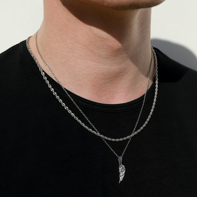 Puede incluir: Un collar de cadena de plata con un colgante de ala de plata. El collar est&aacute; superpuesto con una segunda cadena m&aacute;s fina.