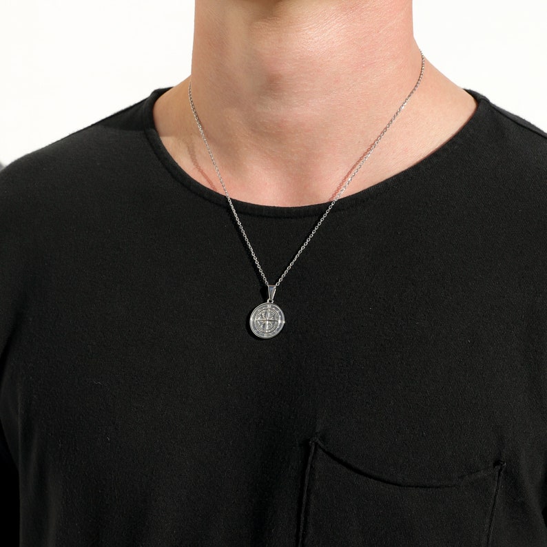 May include: A silver chain necklace with a round pendant featuring a detailed design. The pendant is hanging on a silver chain.